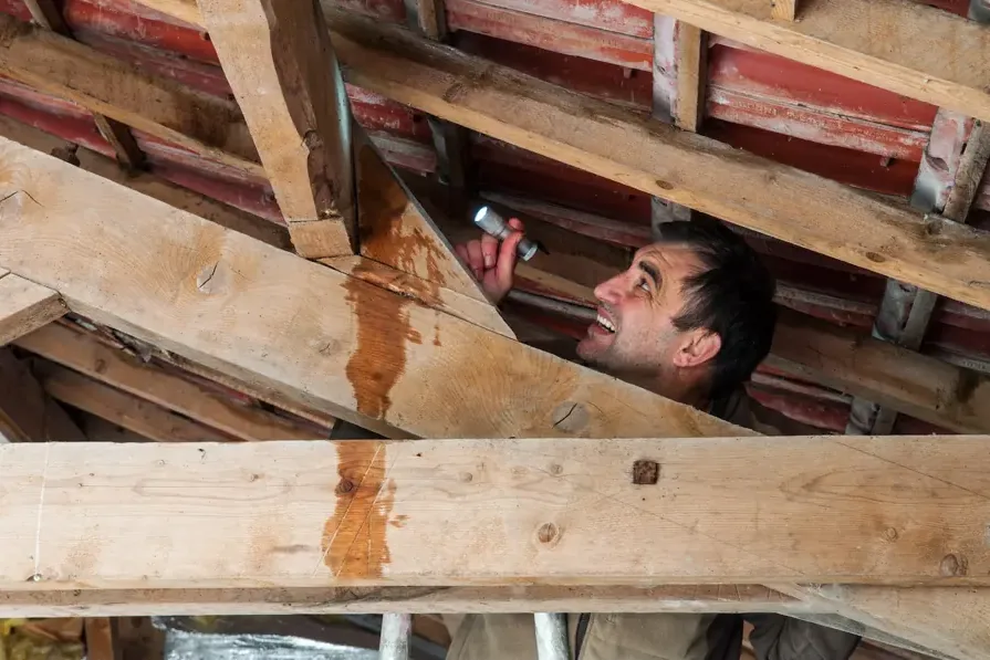 Inspector checking water stains on attic rafters after a roof leak