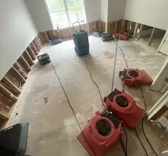 Air movers and a dehumidifier drying a room after flood cuts